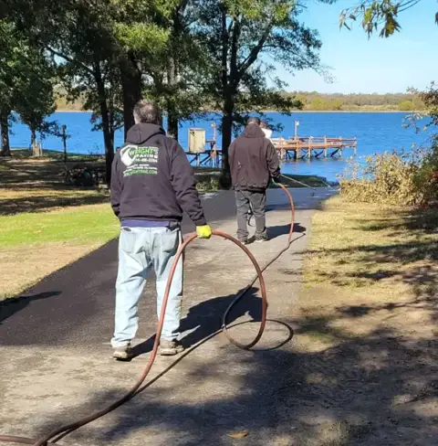Wright's Paving workers apply sealcoating to an asphalt walkway in a park.